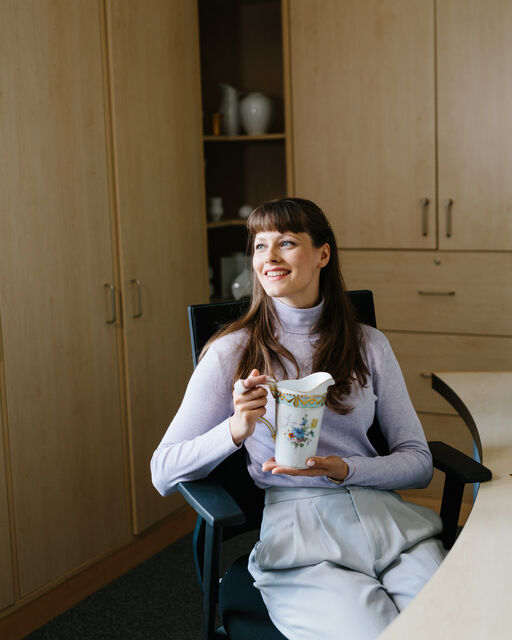 KPM-Mitarbeiterin Marleen Haman an ihrem Bürotisch sitzend mit einem bemalten KURLAND Wasserkrug in Händen