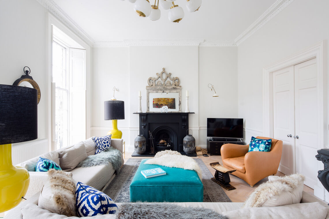 Wohnzimmer mit großem Sofa, bunten Hockern, apricotfarbenem Ohrensessel und Kamin