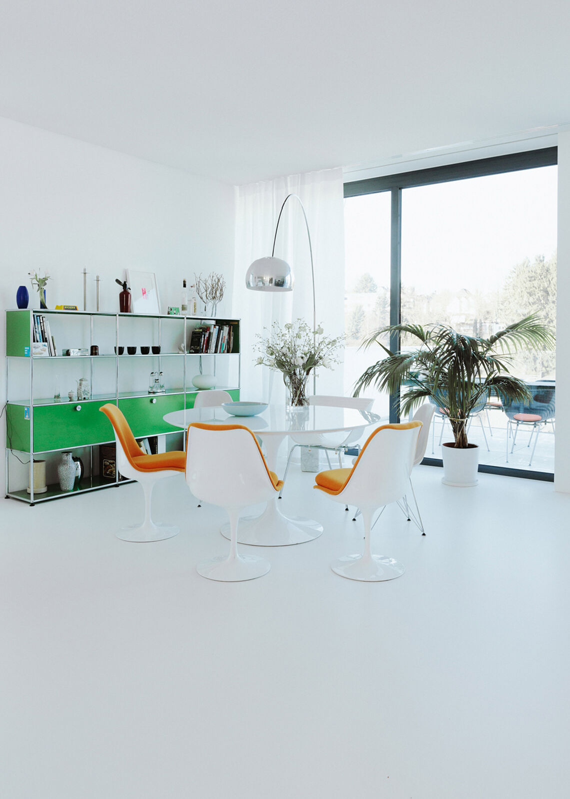 Offener Wohn-Essbereich mit rundem Esstisch, orangefarbenen Stühlen und grünem USM-Regal