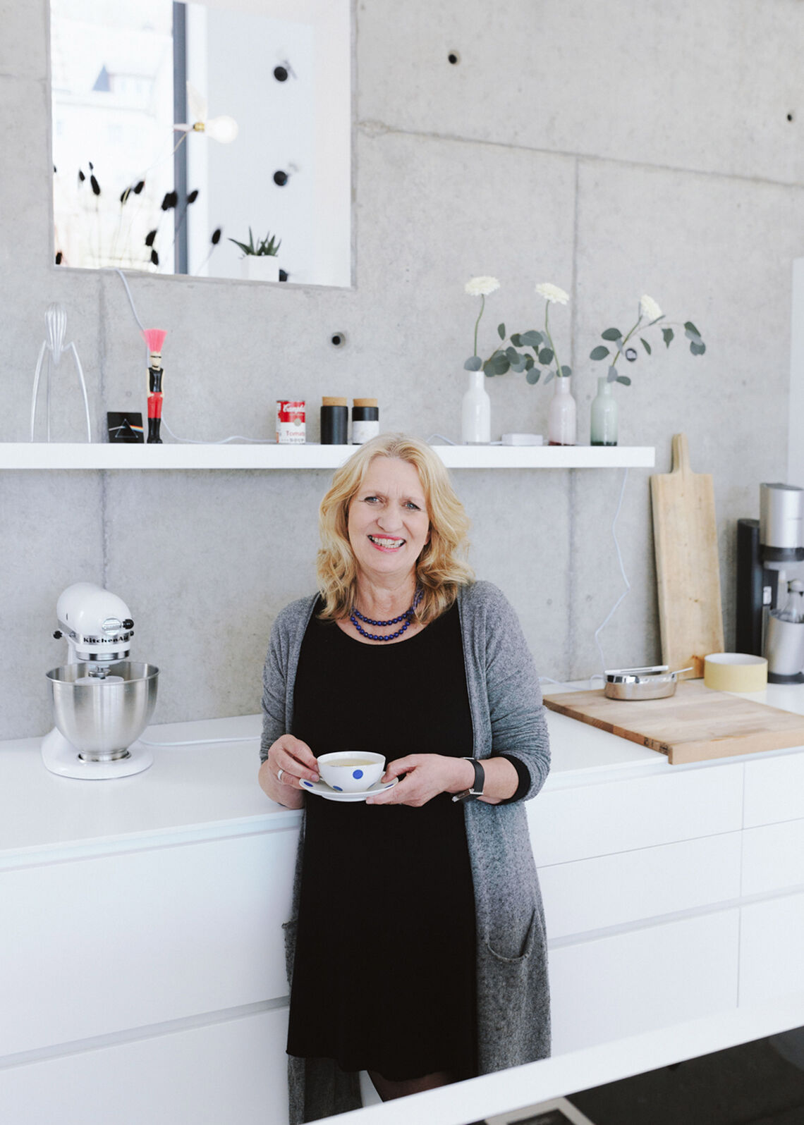 Blonde Frau mittleren Alters steht in moderner Küche und hält eine Tasse in der Hand