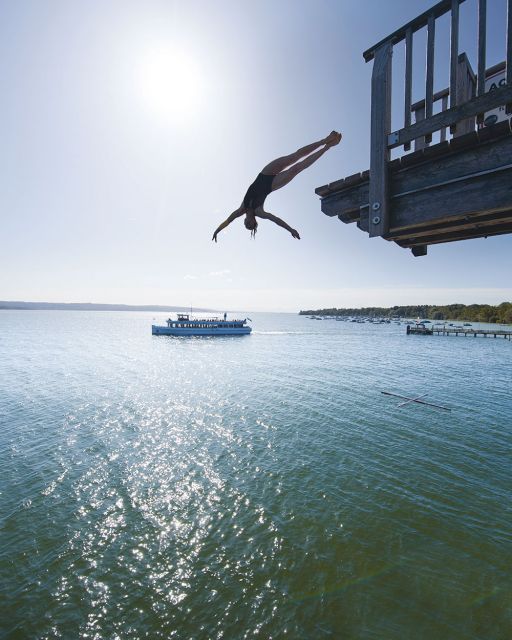 Iris Schmidbauer springt von einem Turm im Hintergrund Schiff auf dem Ammersee