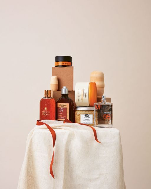 Stillleben mit beigem Stoff, orangenem Geschenkband und Beauty-Produkten vor beigem Hintergrund