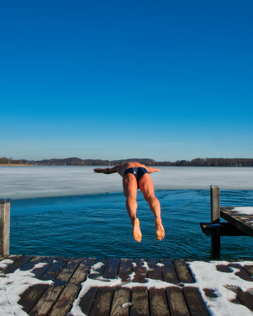 Einer der Winterschwimmer springt vom schneebedeckten Steg in den Wörthsee