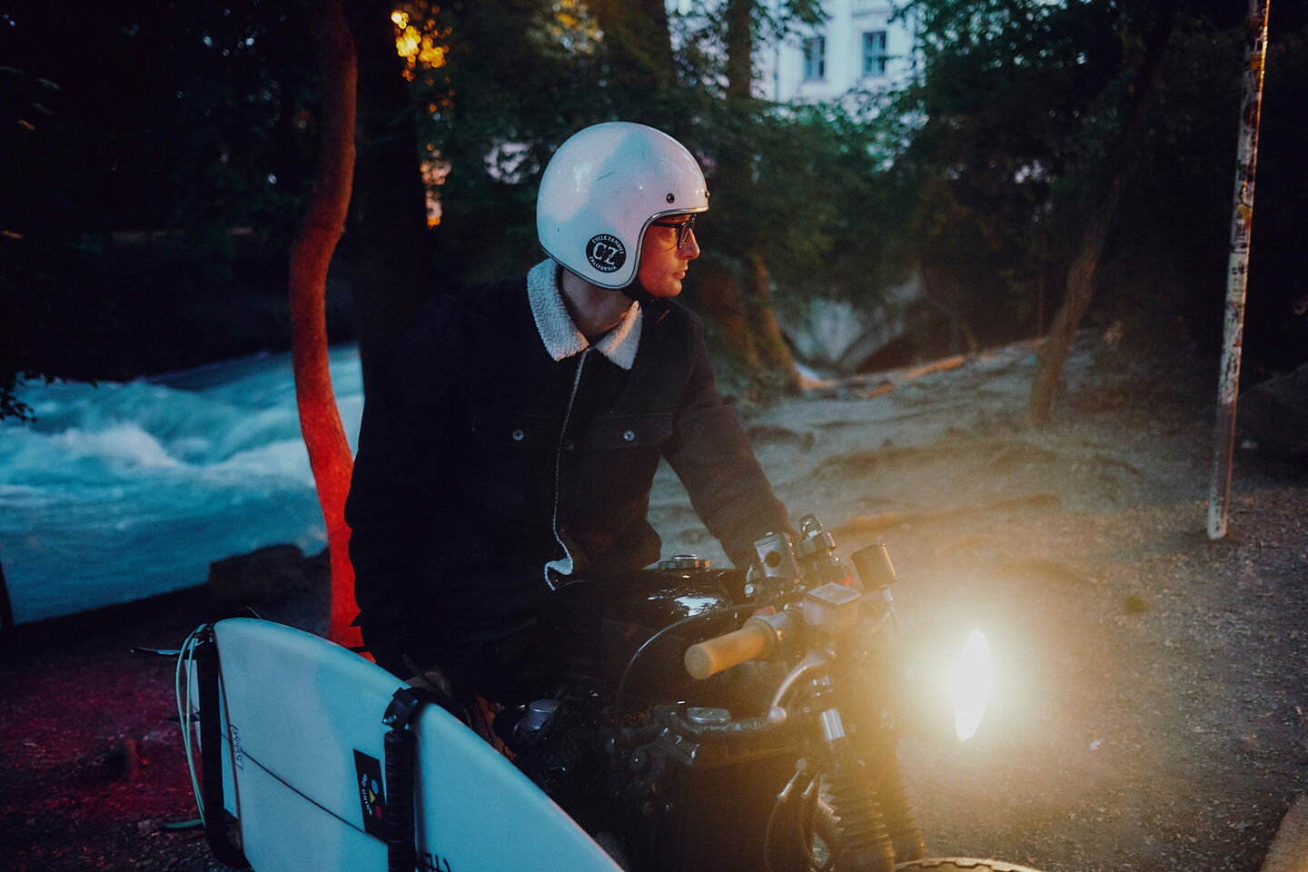 Sebastian Kuhn sits with his surfboard on a motorcycle at dawn