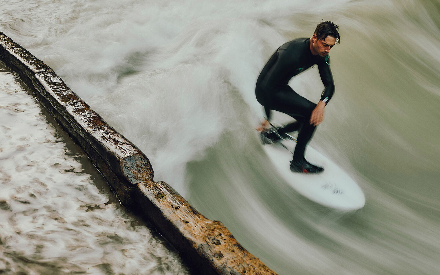 Sebastian Kuhn steht auf seinem Surfbrett und surft die Münchner Eisbachwelle