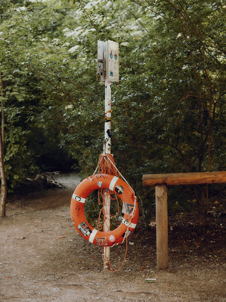 Orange life belt hangs from a white sign with trees in the background