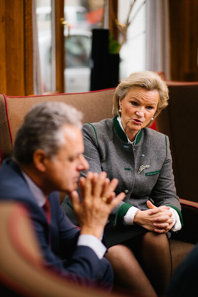 Angela Inselkammer im Hintergrund spricht, während Harald Pechlaner im Vordergrund sitzt, die Hände zusammengefaltet vor dem Gesicht