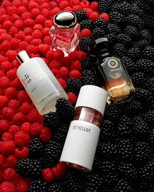 Four perfumes are arranged on raspberries and blackberries.