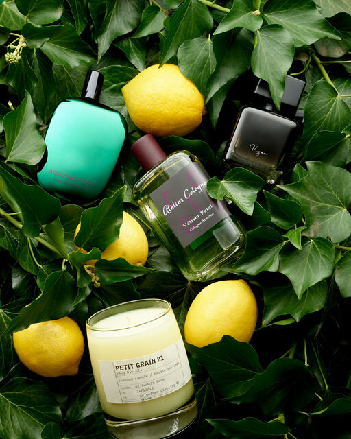 Three perfumes and two lemons lie on a bed of lemon leaves.