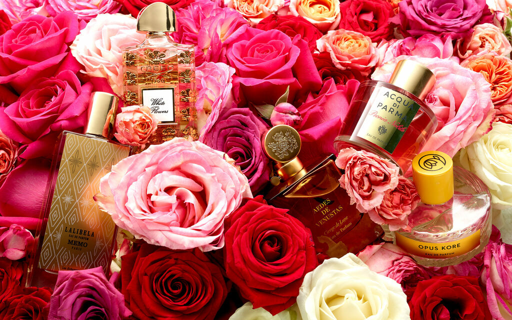 Mehrere Parfüms sind auf einem Bett aus roten, weißen und rosa Rosen inszeniert.