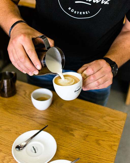 Detailaufnahme bei der Kaffeezubereitung: Milchschaum wird in eine Tasse eingefüllt