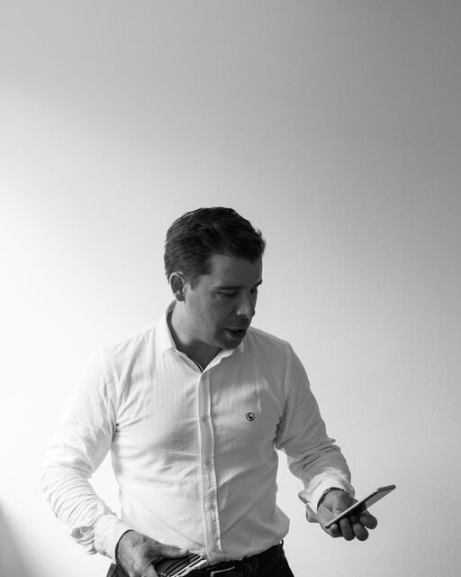 Schwarz-weiß-Aufnahme von Felix Haas, der zwei Handys in den Händen hält und auf den Bildschirm von einem Handy schaut