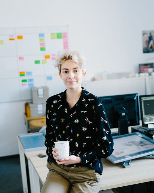 KPM employee Celina van Dyck half-seated on her office desk, holding the LAB cup No. 2H