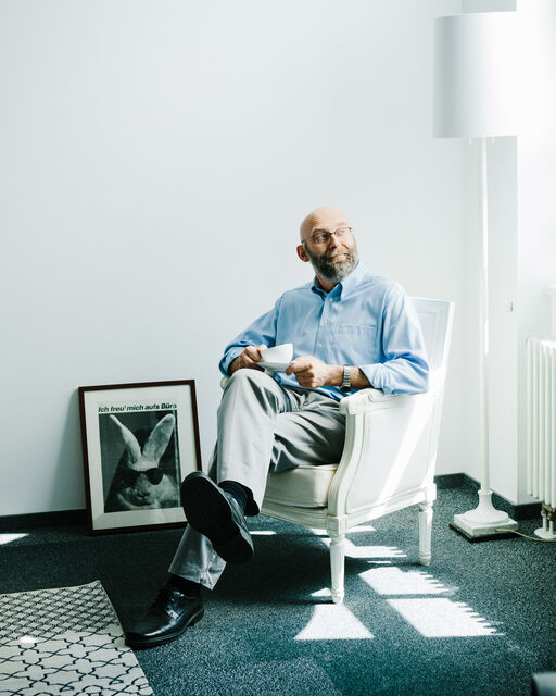 KPM employee Frank Haase sitting in a white reading chair with a KPM breakfast cup