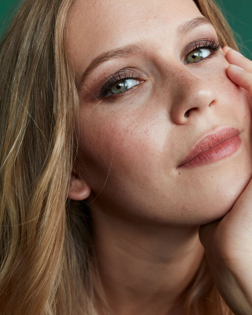 Close-up of a young woman with natural make-up, supporting her chin on her left hand