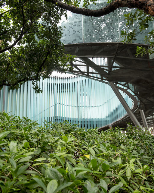 Innenhof eines futuristischen Gebäudes mit geschwungener Glaswand inmitten von Bäumen und Büschen