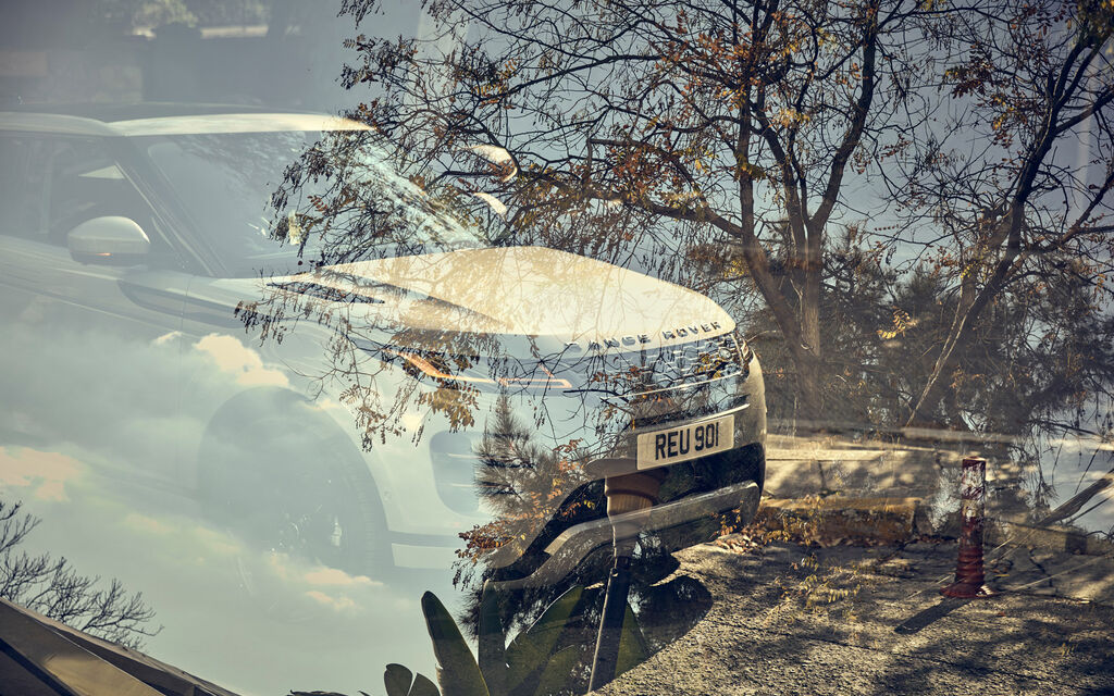 Range Rover Evoque auf Straße mit Olivenbäumen spiegelt sich in Scheibe eines anderen Pkw