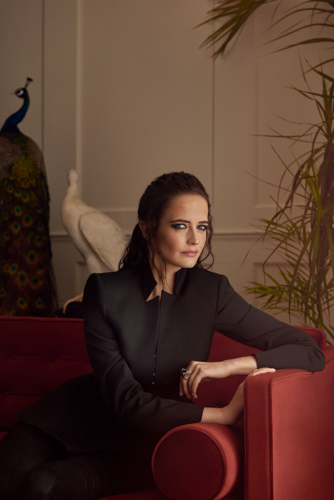 Eva Green wearing a black blouse siting on a red sofa