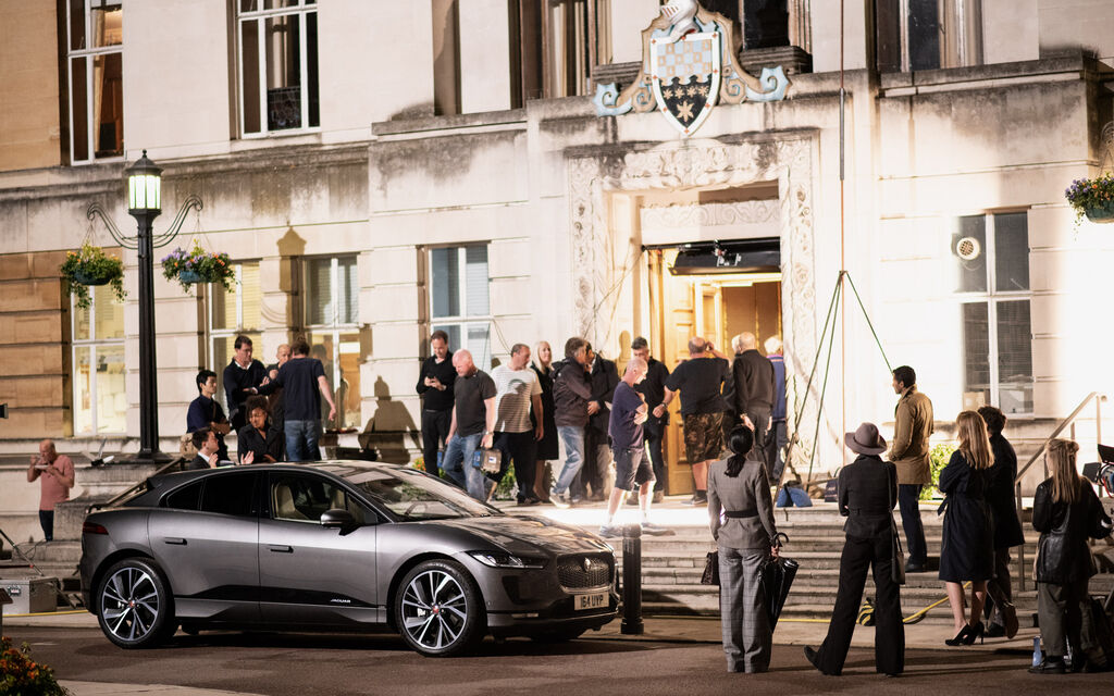 Grey Jaguar I-PACE stands surrounded by several people in front of building