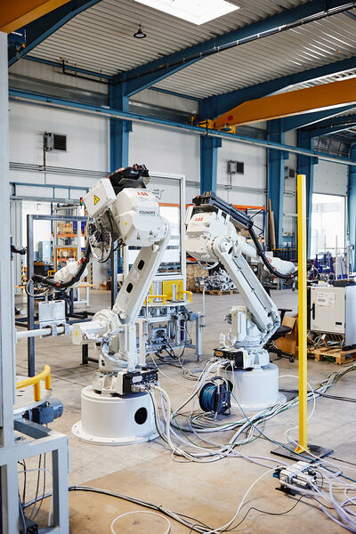Two industrial robots with several cables are in the production hall of Main-Automatik
