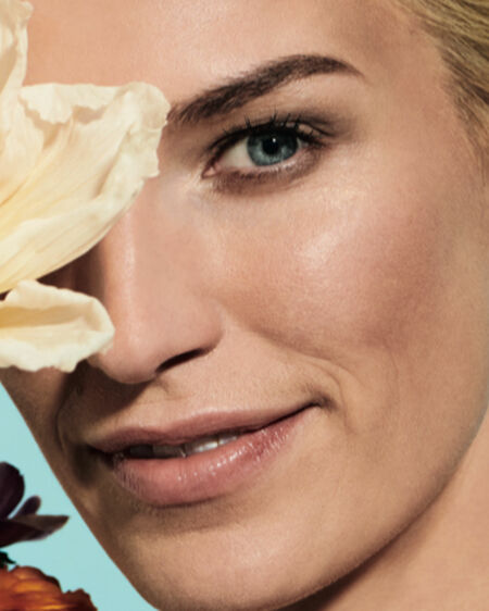 Naturally made-up woman with blond short hair and yellow blossom in front of the right eye