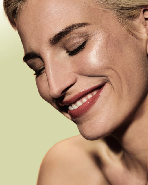 Close-up einer dezent geschminkten, lächelnden Frau mit geschlossenen Augen