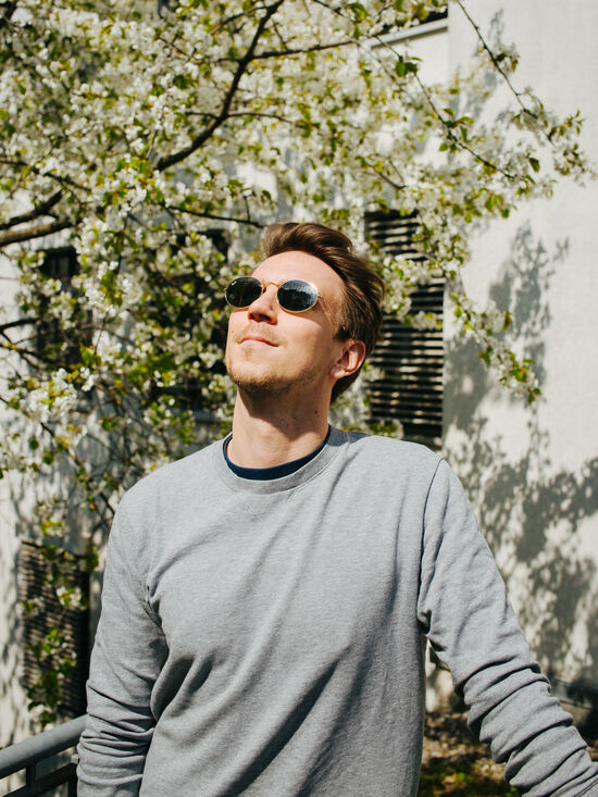 Start-up founder Daniel Schmitt wears sunglasses and gazes into the sun in front of a blossoming cherry tree