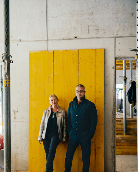 Architect couple Ina and Gunther Laux standing in front of a yellow wooden wall