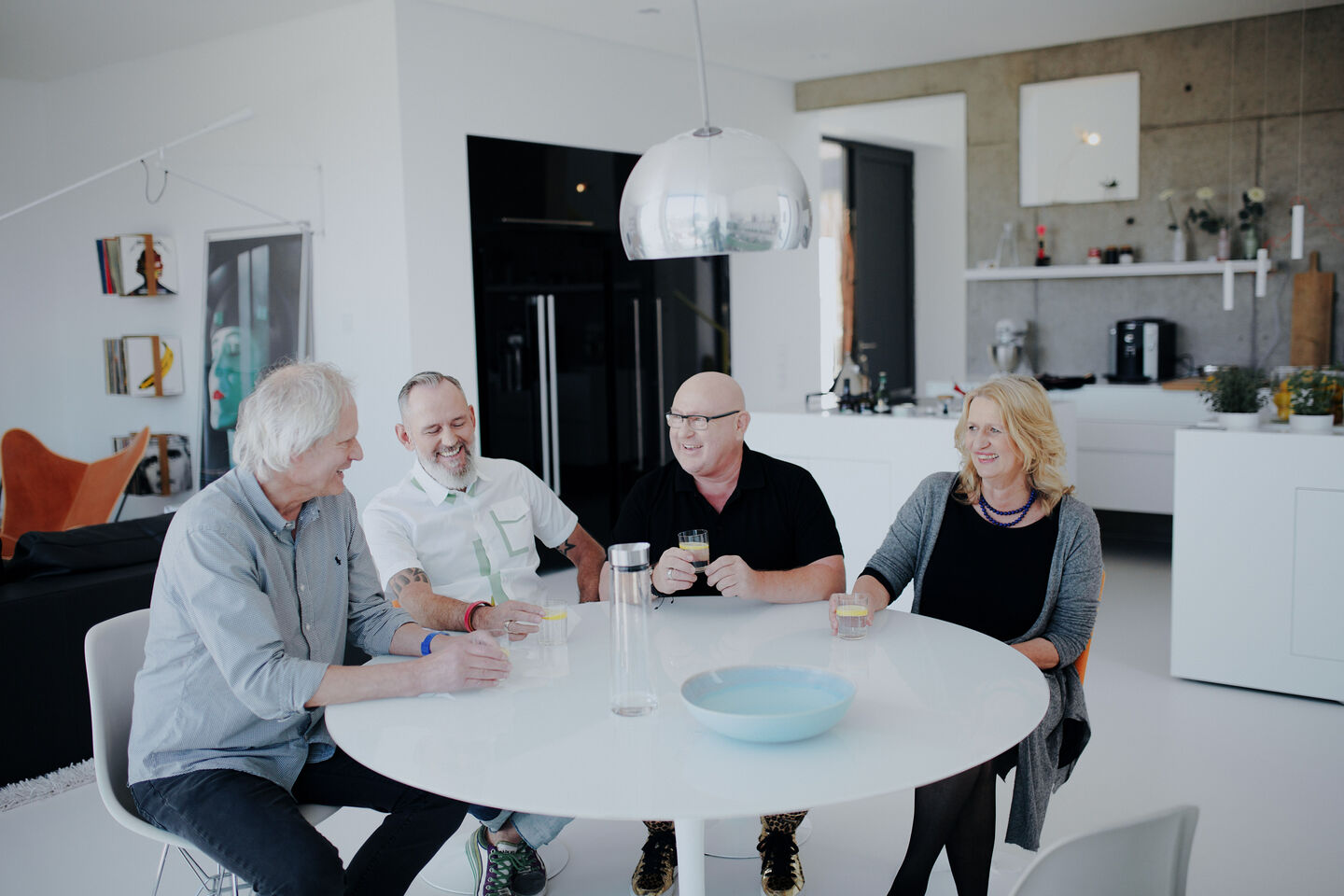 Drei Männer und eine Frau sitzen an einem runden Esstisch in einer Küche zusammen
