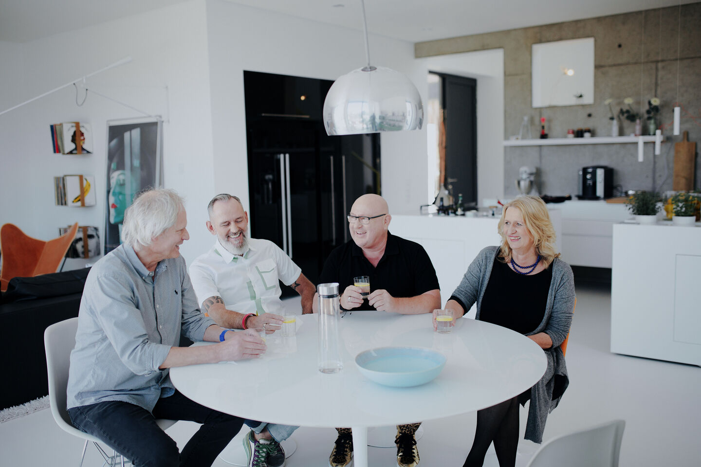 Three men and one woman sitting together at a round dining table in a kitchen