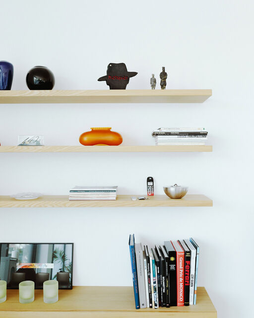 Three shelves with decoration hang on wall above chest of drawers with coffee table books