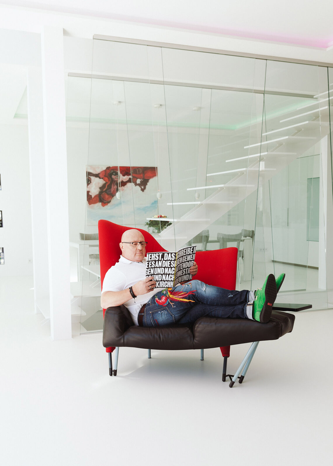 Bald man sitting on red-black armchair reading a magazine