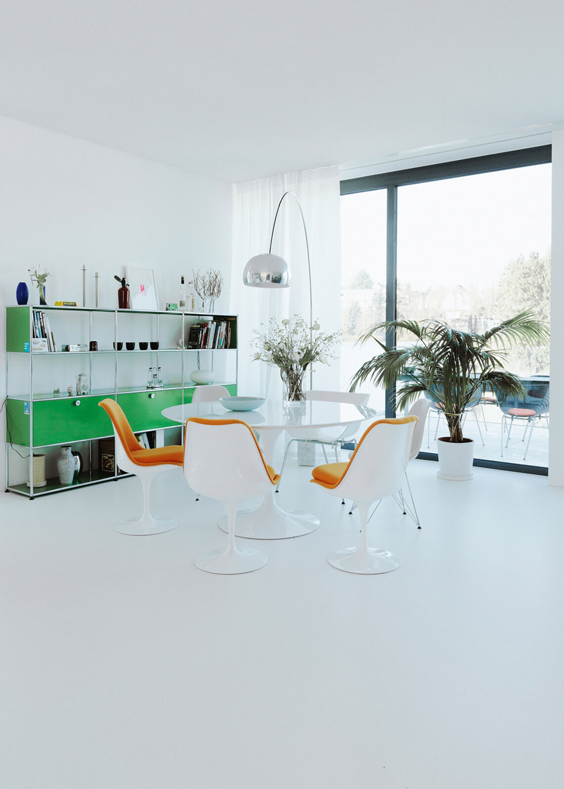 Open living/dining area with round dining table, orange chairs and green USM shelf