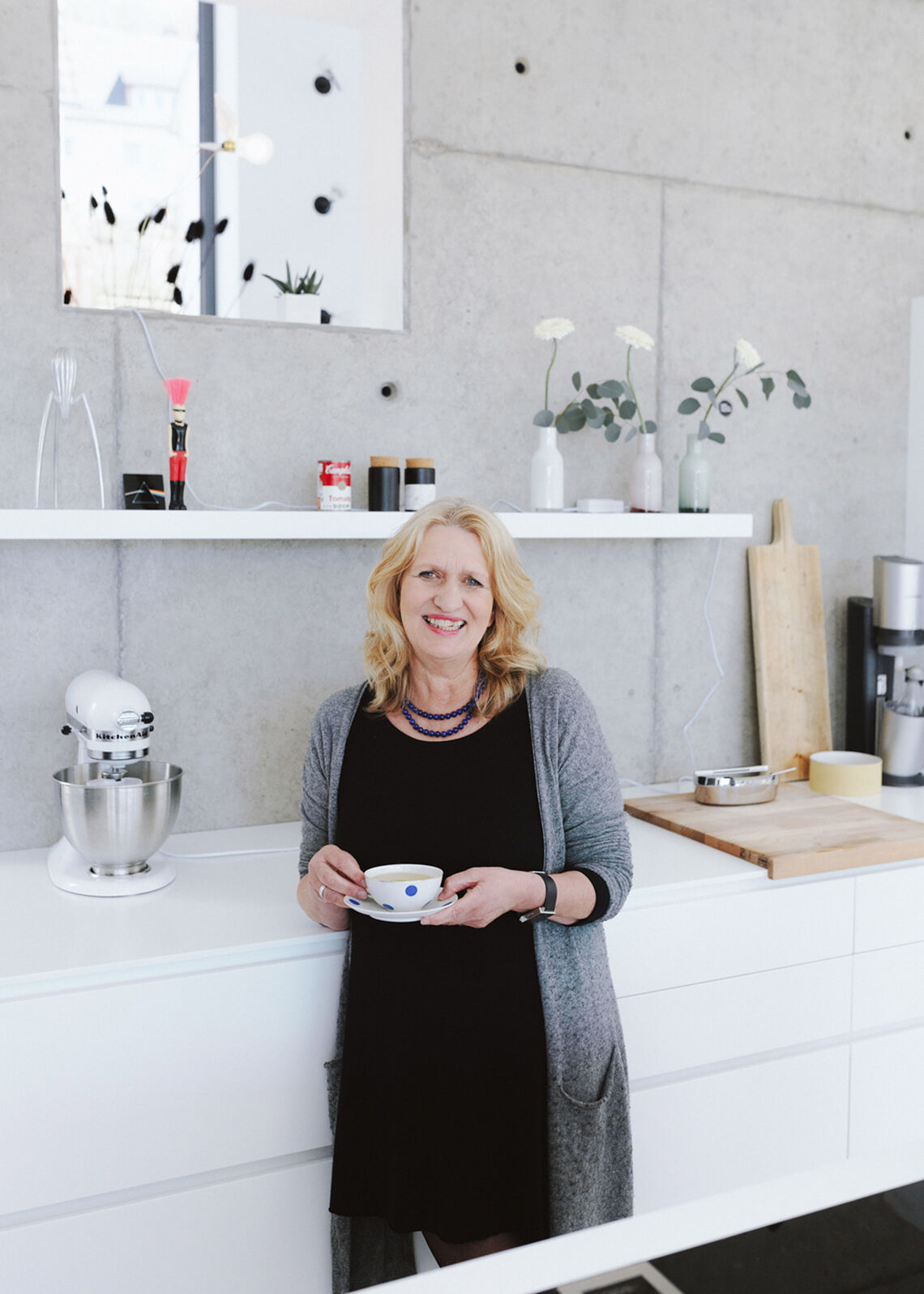 Middle-aged blonde woman stands in modern kitchen and holds a cup in her hand