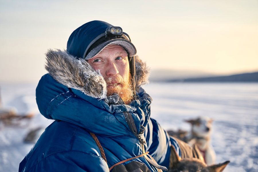 Portrait photo of dog sledge driver Jonas in blue winter coat with fur collar at sunset