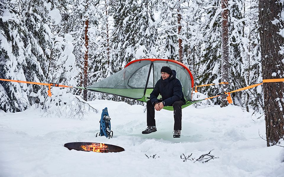Mann sitzt im schneebedeckten Wald vor Feuerstelle