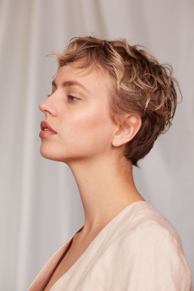 Seitliche Aufnahme einer jungen Frau mit kurzen Haaren und natürlichen Makeup vor weißem Hintergrund