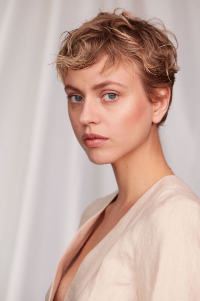 Nahaufnahme einer jungen Frau mit kurzen Haaren und natürlichen Makeup vor weißem Hintergrund