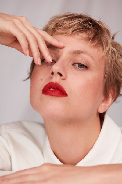 Young woman in white jeans jacket wearing makeup and red lipstick against white background