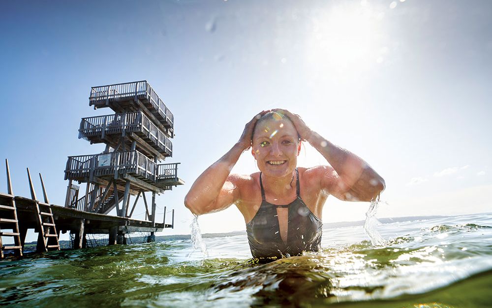 Iris Schmidbauer taucht aus dem Ammersee auf. Im Hintergrund Sprungturm des Strandbad Utting