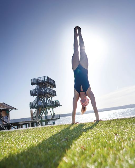 Iris Schmidbauer macht einen Handstand vor einem Sprungturm am Ammersees