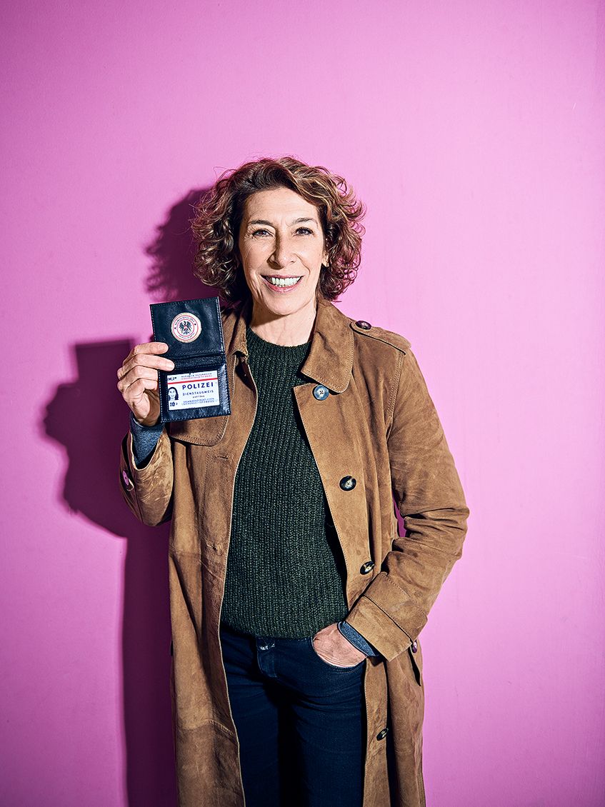 Portrait of Adele Neuhauser with badge in front of a pink wall