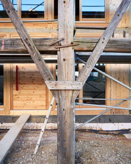 Holzgebälk steht vor Holzscheune mit Baugerüst