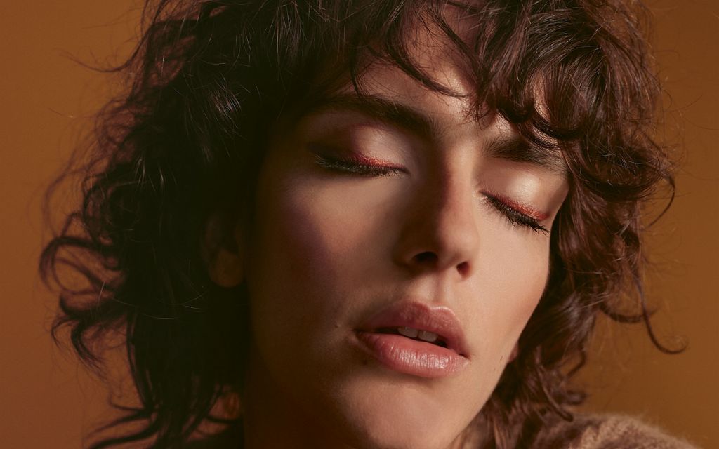 Young woman with brown curls with closed eyes on the lids is a copper colored eyelid line