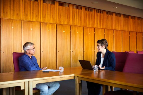 Stefan Ruzas und Veronika Grimm sitzen sich am Tisch gegenüber