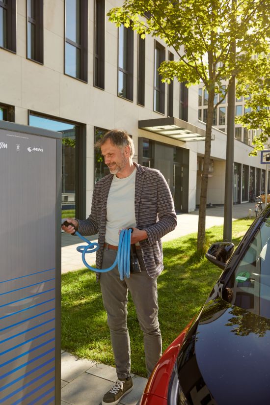 Mann steht vor einer Ladestation für Elektrofahrzeuge mit Kabel in der Hand