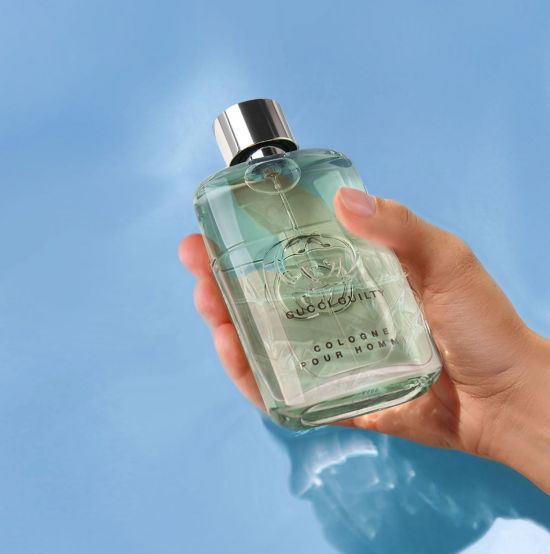 Hand hält Parfum „Gucci Guilty Cologne Pour Homme” vor blauem Hintergrund