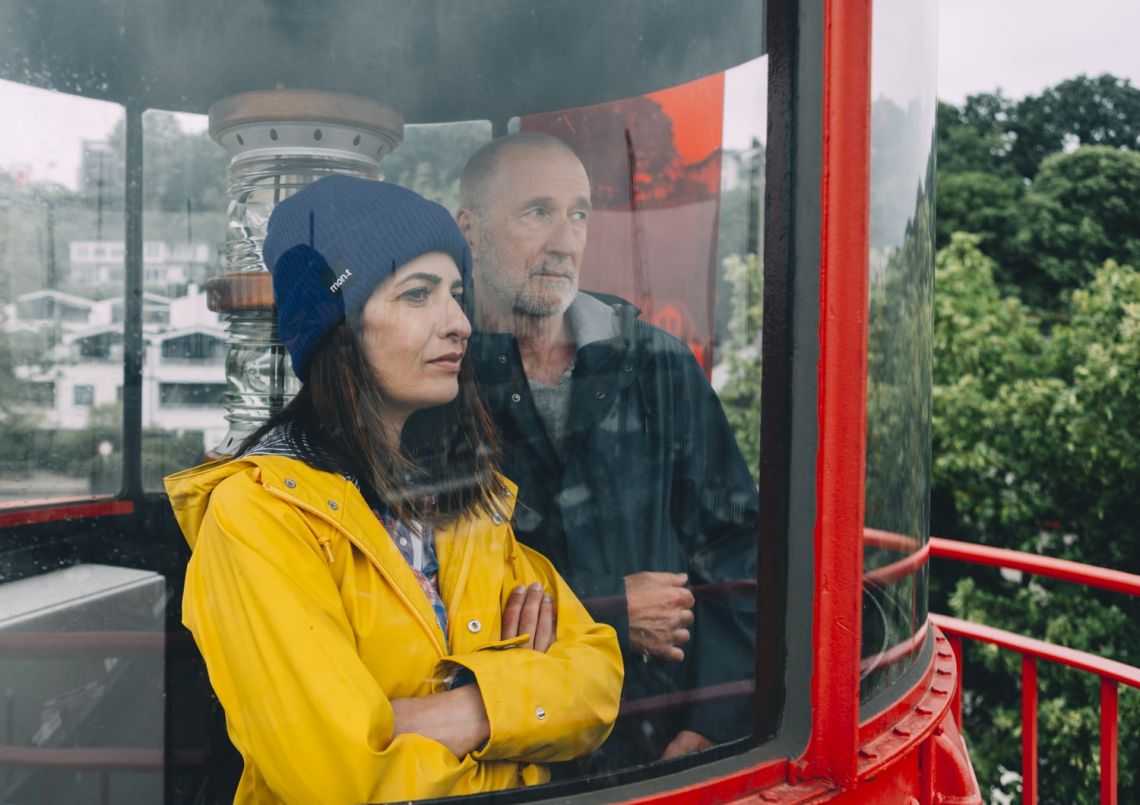 Linda Zervakis und Peter Lohmeyer stehen am Fenster eines Leuchtturms