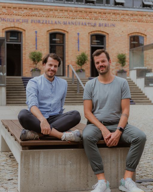 Zwei Männer sitzen lächelnd im Hof der KPM Berlin