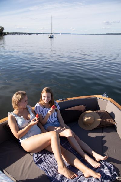 Zwei junge Frauen sitzen in Elektroboot und essen Wassermelone